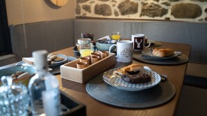 Ein Frühstückstisch mit Steinwand und verschiedenen Speisen, darunter Brot, Gebäck und eine Tasse mit dem Aufdruck "DANDY VILLAGE".