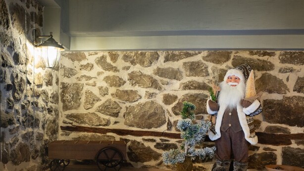Une salle de bain aux murs de pierre, avec une baignoire, une statuette de gnome décorative et un chariot en bois.