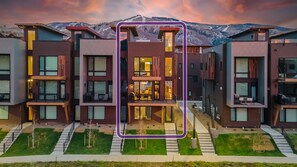 Um edifício residencial moderno de vários andares, com amplas janelas, um pátio central e vista para montanhas ao fundo.