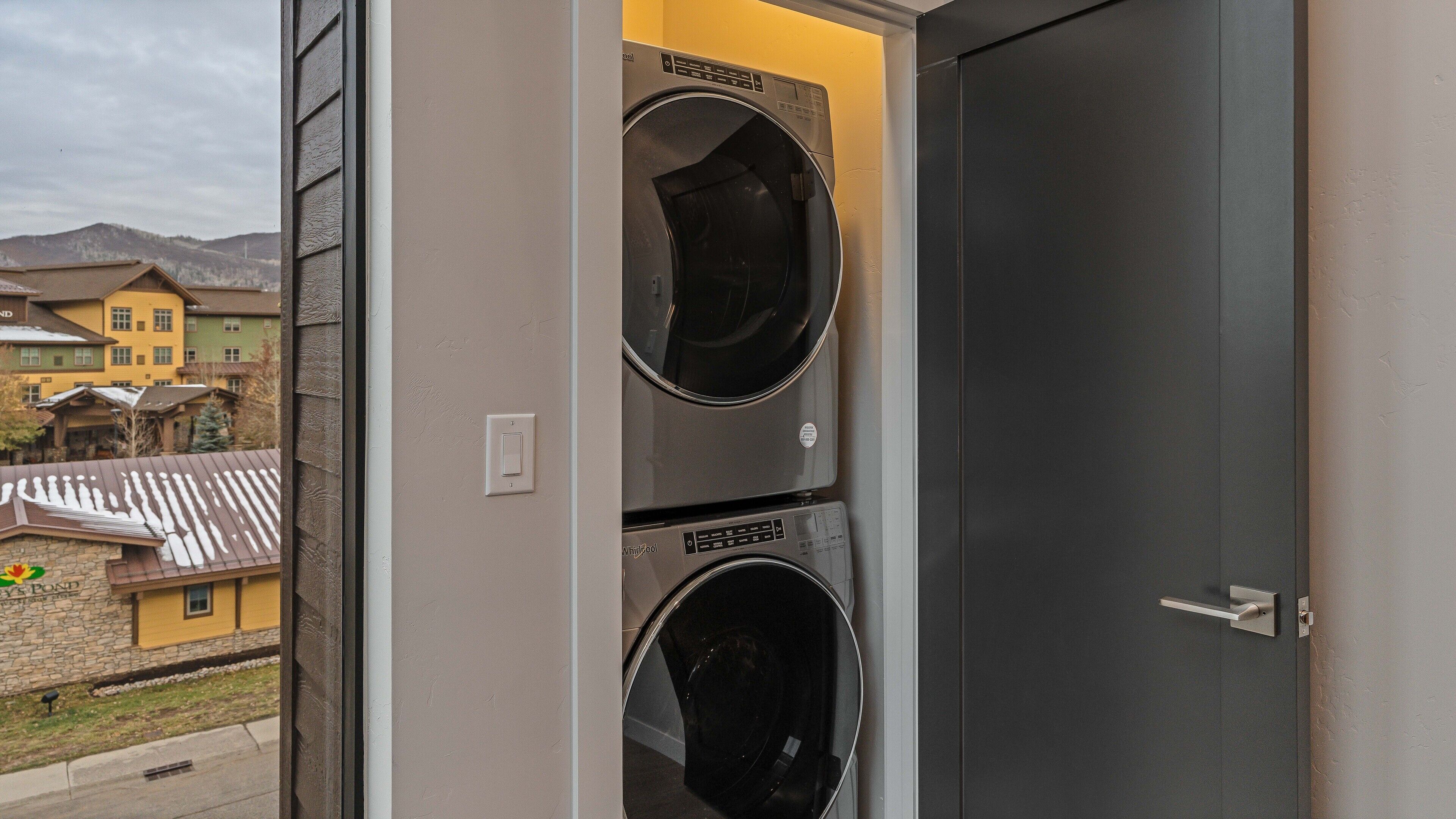 A laundry room with two stacked washers and dryers, a door, and a view of buildings outside.
