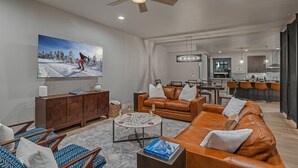 Een moderne woonkamer met een grote flatscreen-televisie, leren banken, een salontafel en een eethoek met barstoelen.