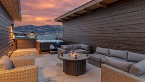 Een terras buiten met een hottub, zithoek en uitzicht op de bergen.