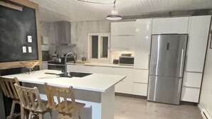 Eine moderne Küche mit einer zentralen Kochinsel, Holzsesseln und einem Edelstahl-Kühlschrank.