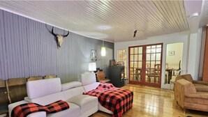 Ein Wohnzimmer mit einem weißen Sofa, einer karierten Decke, einem Fellteppich und einem Kamin aus Stein.