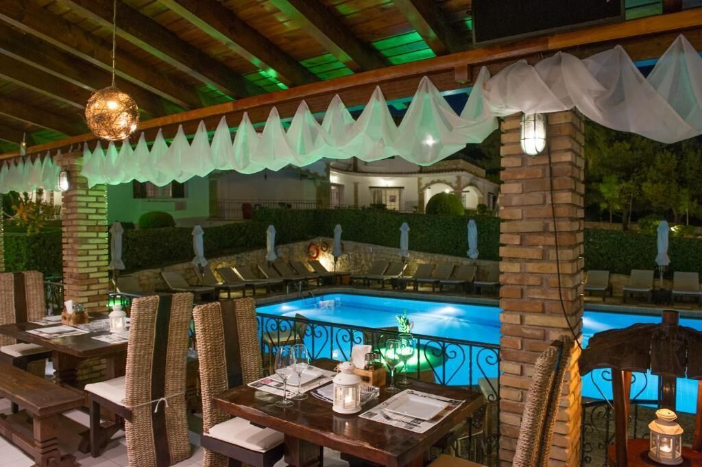Un área de comedor al aire libre con mesas y sillas, una piscina y un espacio de estar cubierto con vista a la piscina.