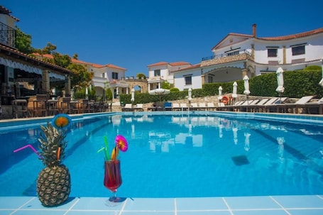 A swimming pool with lounge chairs and umbrellas, surrounded by buildings with red-tiled roofs.