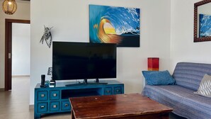 Ein Wohnzimmer mit Flachbildfernseher, Couchtisch aus Holz, einem blauen Schrank und einer Couch mit blauen Kissen.