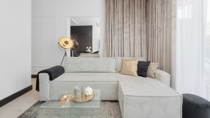 A modern living room with a sectional sofa, a glass coffee table, and a large window with curtains. - Tastefully Arranged Studio by Renters (Wroclaw)