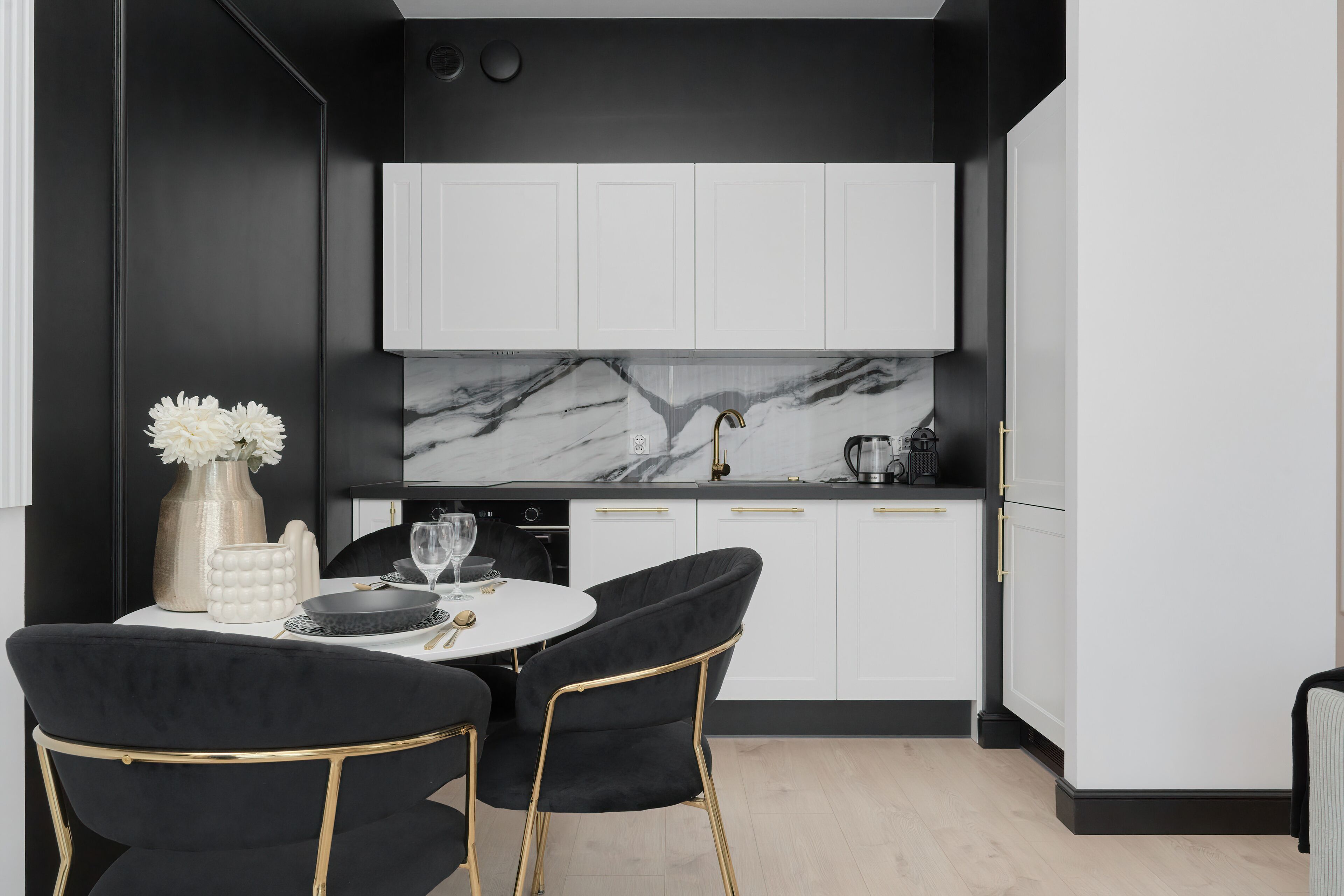 A modern kitchen with white cabinets, a marble backsplash, and a black dining area with two chairs.