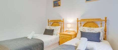 Een hotelkamer met twee eenpersoonsbedden, elk met een houten hoofdeinde, een nachtkastje met een lamp en een kleine tafel.