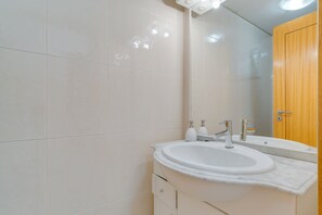 Un baño con azulejos blancos, un lavabo blanco y una puerta de madera.