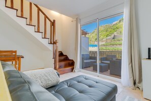 Un salon moderne avec un canapé gris, un escalier en bois et un balcon agrémenté de mobilier d’extérieur.