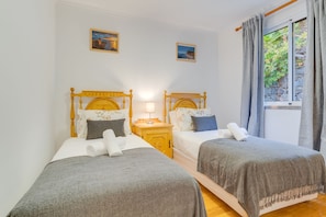 Ein Zimmer mit zwei Betten, einem Nachttisch, einer Lampe und einem Fenster mit Vorhängen.
