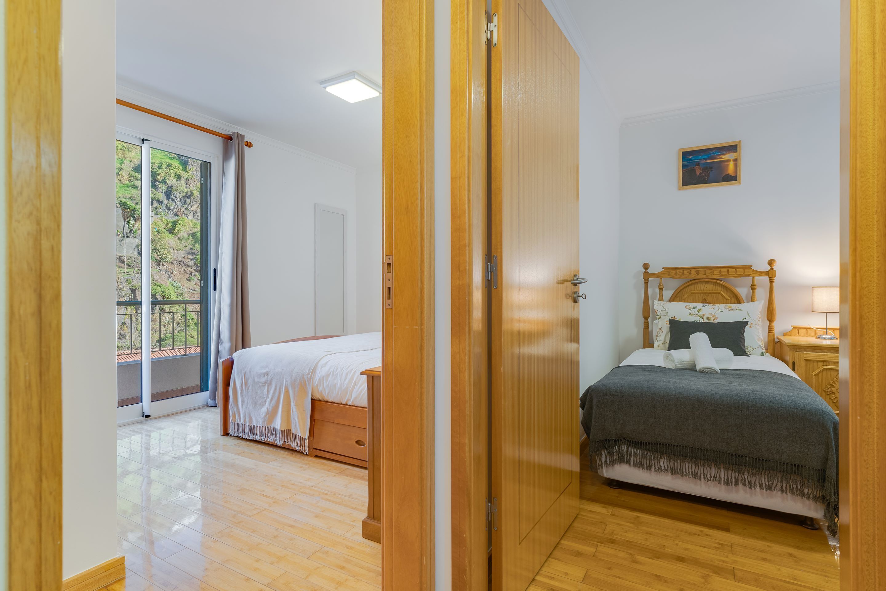A bedroom with a wooden bed, a nightstand, a window with curtains, and a door leading to another room.