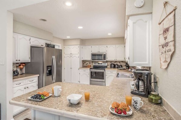 A modern kitchen with white cabinets, stainless steel appliances, and a breakfast setup on the counter.
