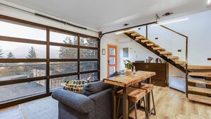 A modern interior with a large window, a wooden staircase, a dining area, and a cozy seating area.