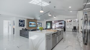 A modern kitchen with a large island, stainless steel appliances, and a seating area with a gray sofa. - Kayaks, Boat Dock, Heated Pool & Spa, Outside Kitchen, Tiki Hut - Villa Pedro - Roelens Vacations (Cape Coral)