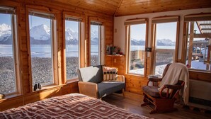 A cozy cabin with wooden walls and large windows overlooking a snowy landscape. - Rustic Roots Seaside Blush Cabin (ADA) (Seward)