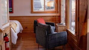 A cozy cabin interior with a wooden ceiling, a bed, a desk, and a chair. - Rustic Roots Seaside Cardinal Cabin (Seward)