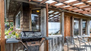 A wooden deck with a grill, chairs, and a view of the ocean. - Rustic Roots Seaside Cardinal Cabin (Seward)