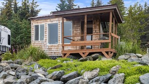 A wooden cabin with a porch, surrounded by rocks and greenery. - Rustic Roots Seaside Indigo Cabin (Seward)