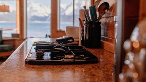 A kitchen with a stove, utensils, and a view of mountains through large windows. - Rustic Roots Seaside Indigo Cabin (Seward)