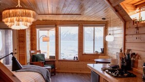 A compact cabin with a bed, a small kitchen, and a view of the lake. - Rustic Roots Seaside Indigo Cabin (Seward)
