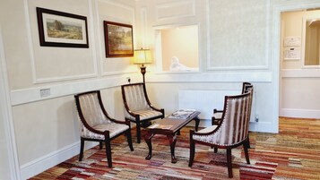 Una habitación con tres sillones tapizados alrededor de una pequeña mesa, una lámpara y obras de arte enmarcadas en la pared.