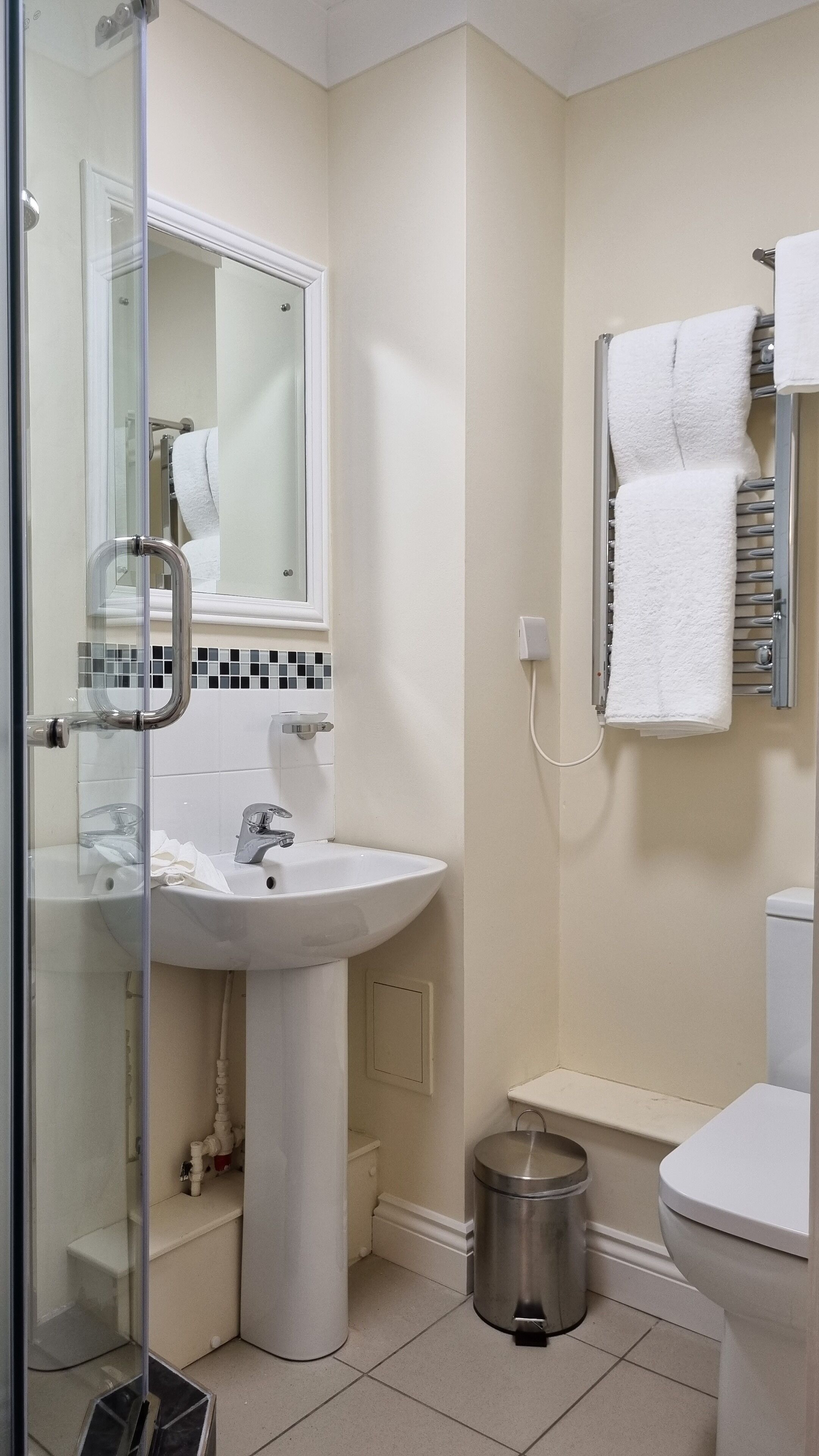 A bathroom with a glass shower enclosure, a white sink, a mirror, a towel rack, and a toilet.