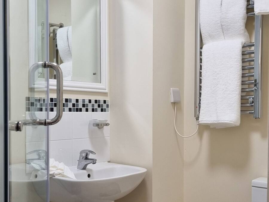 Ein Badezimmer mit Duschkabine aus Glas, Waschbecken in Weiß, Spiegel, Handtuchhalter und Toilette.