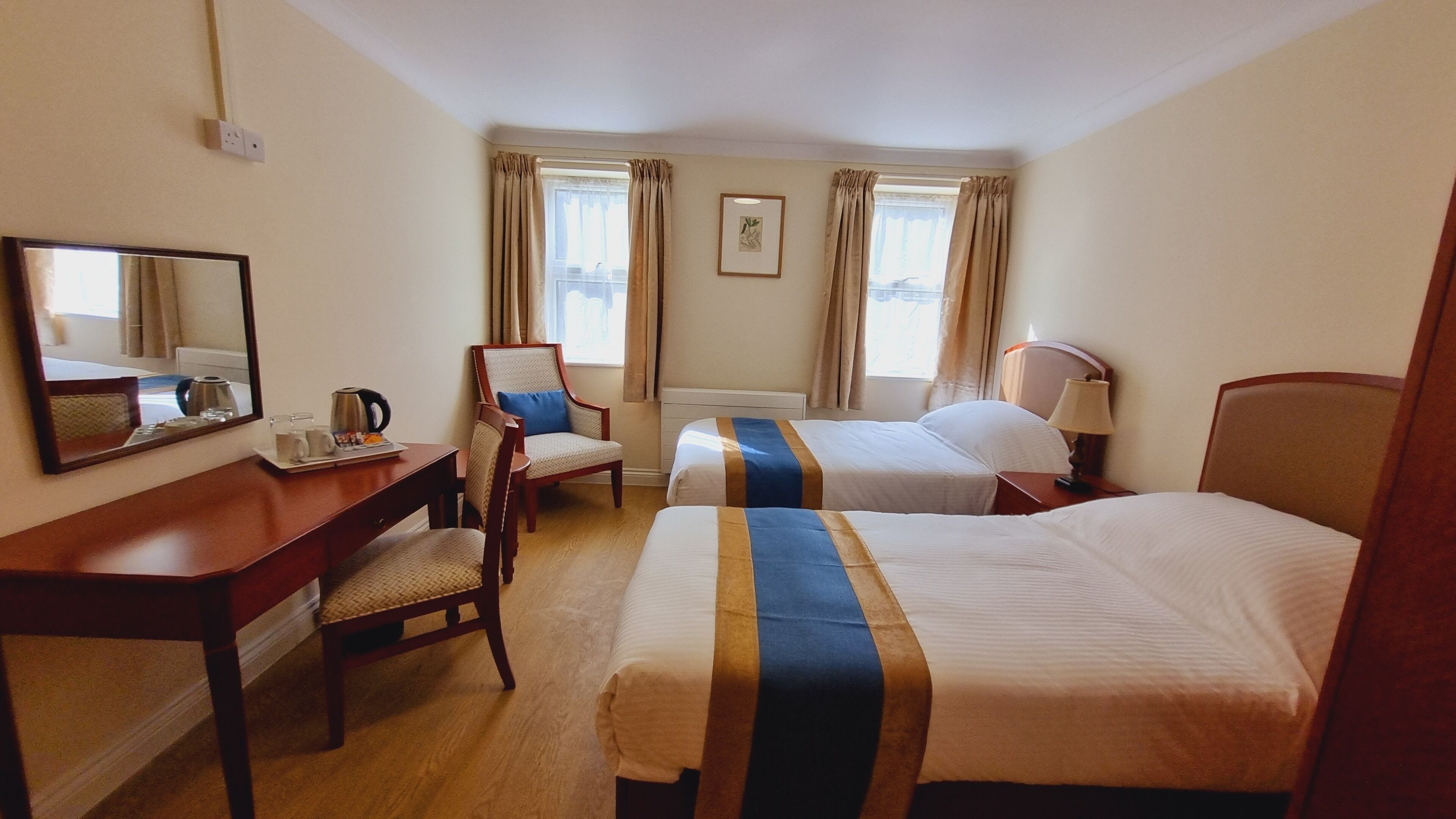 Une chambre d’hôtel avec deux lits, un bureau avec une chaise, un miroir et une fenêtre avec des rideaux.