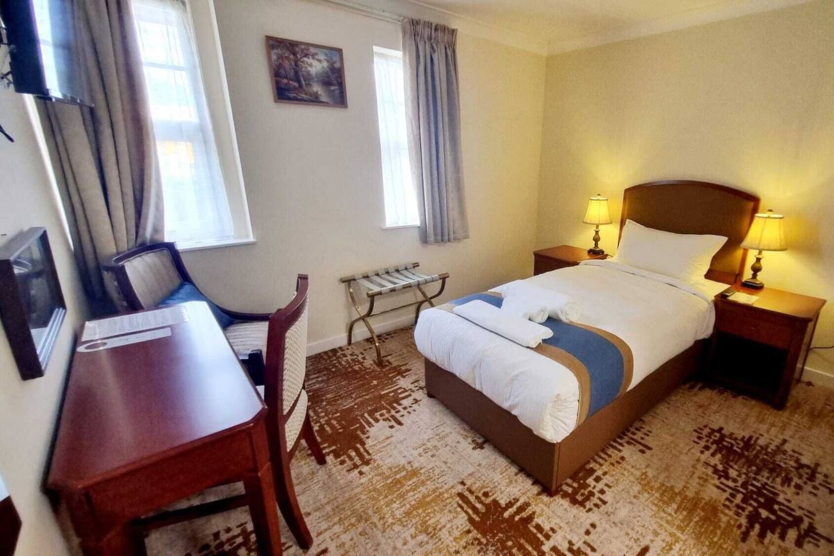 Hotellihuone, jossa on sänky, yöpöytälamput, työpöytä ja tuoli.