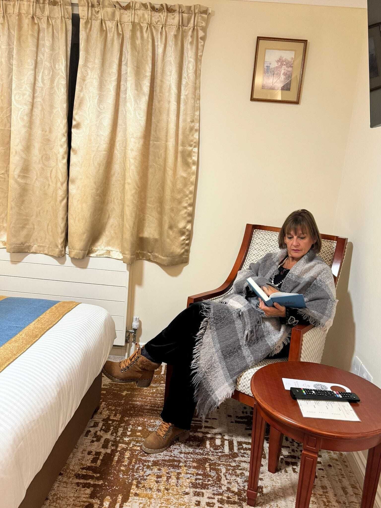 Una habitación con cama, una silla, una mesita y una ventana con cortinas.