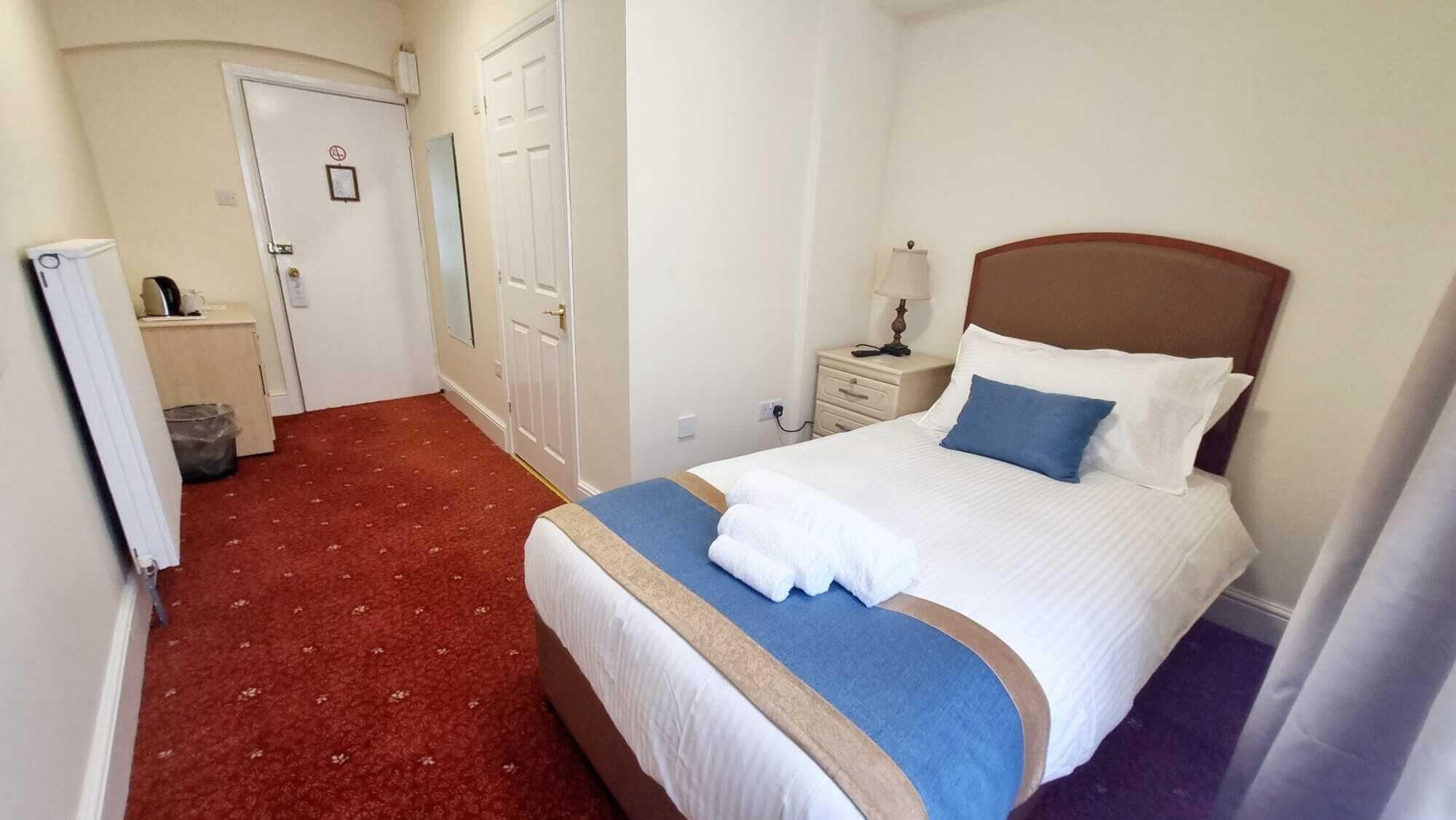 Une chambre d’hôtel avec un lit, une table de chevet, une lampe, un radiateur et une porte.