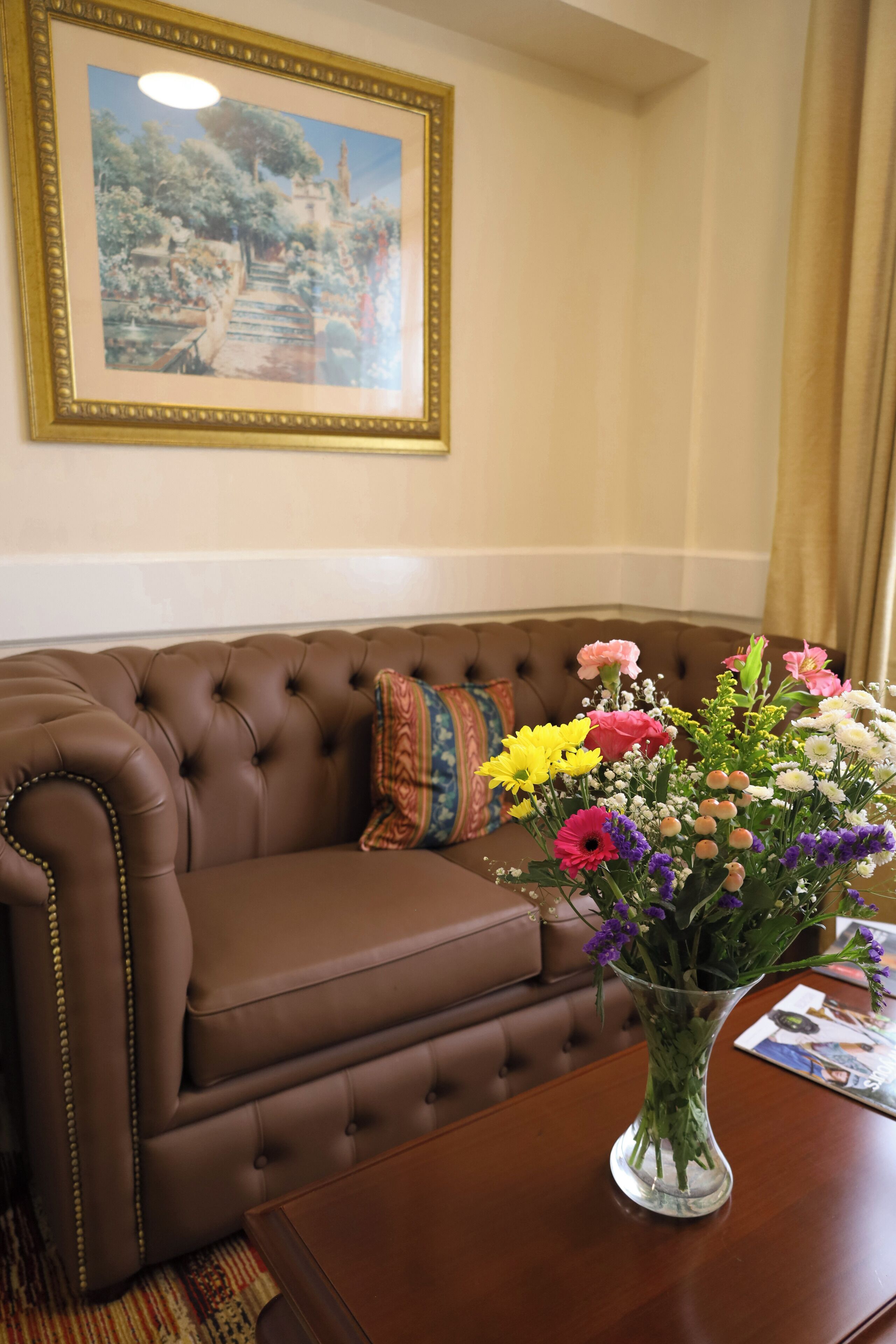 Un sofá de cuero marrón con un jarrón de flores coloridas sobre una mesa de madera.