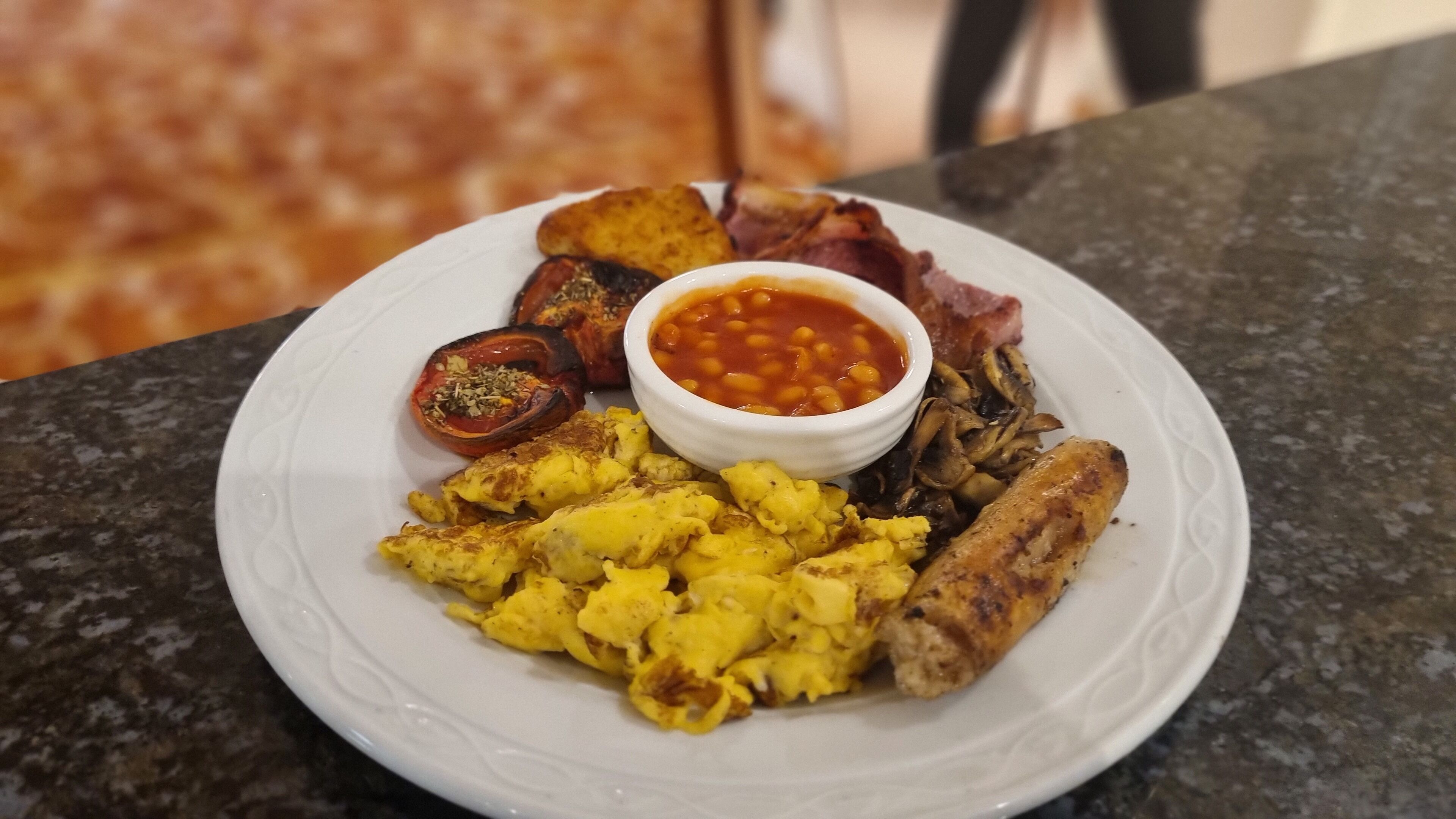 A plate of breakfast food including eggs, sausages, bacon, beans, and a tomato.