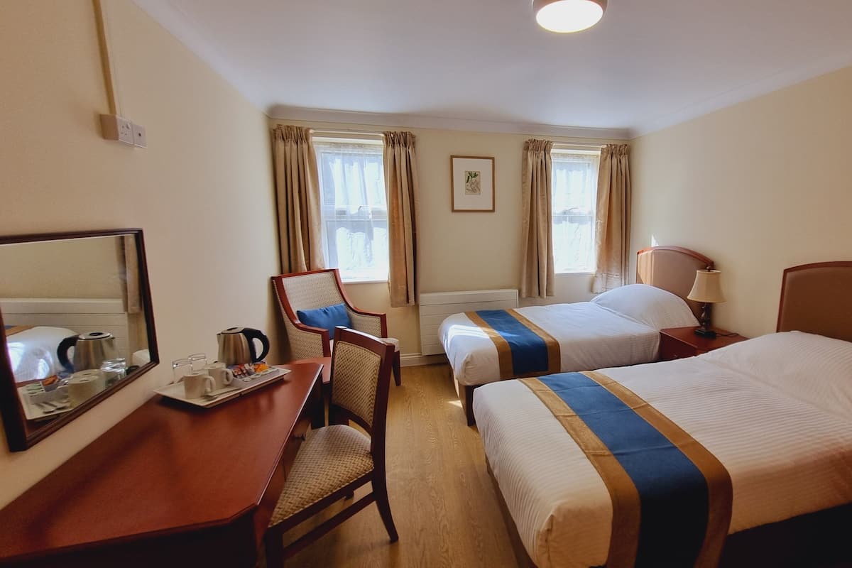 Hotellihuone, jossa on kaksi sänkyä, työpöytä tuolilla, peili ja ikkuna, jossa on verhot.