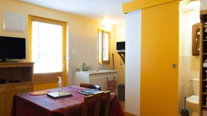 A small, bright room with a dining table, a television, and a bathroom visible through an open door. - Studio Calme Chaleureux (Brive-la-Gaillarde)