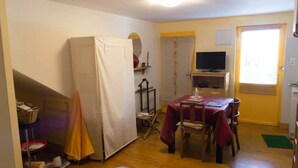 A room with a wooden floor, a table with chairs, a television, a refrigerator, and a window with blinds. - Studio Calme Chaleureux (Brive-la-Gaillarde)