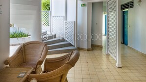 A clean, modern interior with wicker furniture, a staircase leading to an outdoor area, and a blue door in the background. - L'oasis du quai (Saint-François)