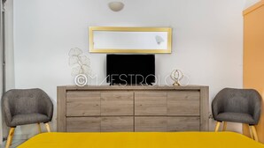 A modern bedroom with a bed, two armchairs, a TV, and a wooden dresser. - L'oasis du quai (Saint-François)