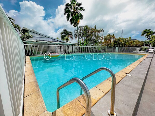 A swimming pool with clear blue water, surrounded by a white fence and palm trees.