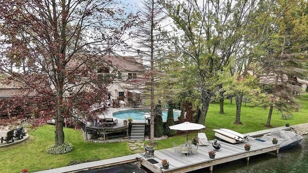 Une propriété au bord du lac, dotée d’un quai, d’un bateau appelé « MasterCraft », d’une piscine et d’un espace patio aménagé avec du mobilier d’extérieur.