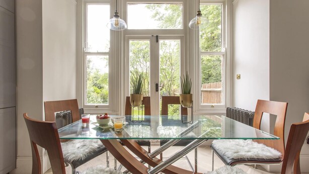 Un espace repas avec une table en verre, des chaises en bois et une vue sur la verdure grâce à de grandes fenêtres.