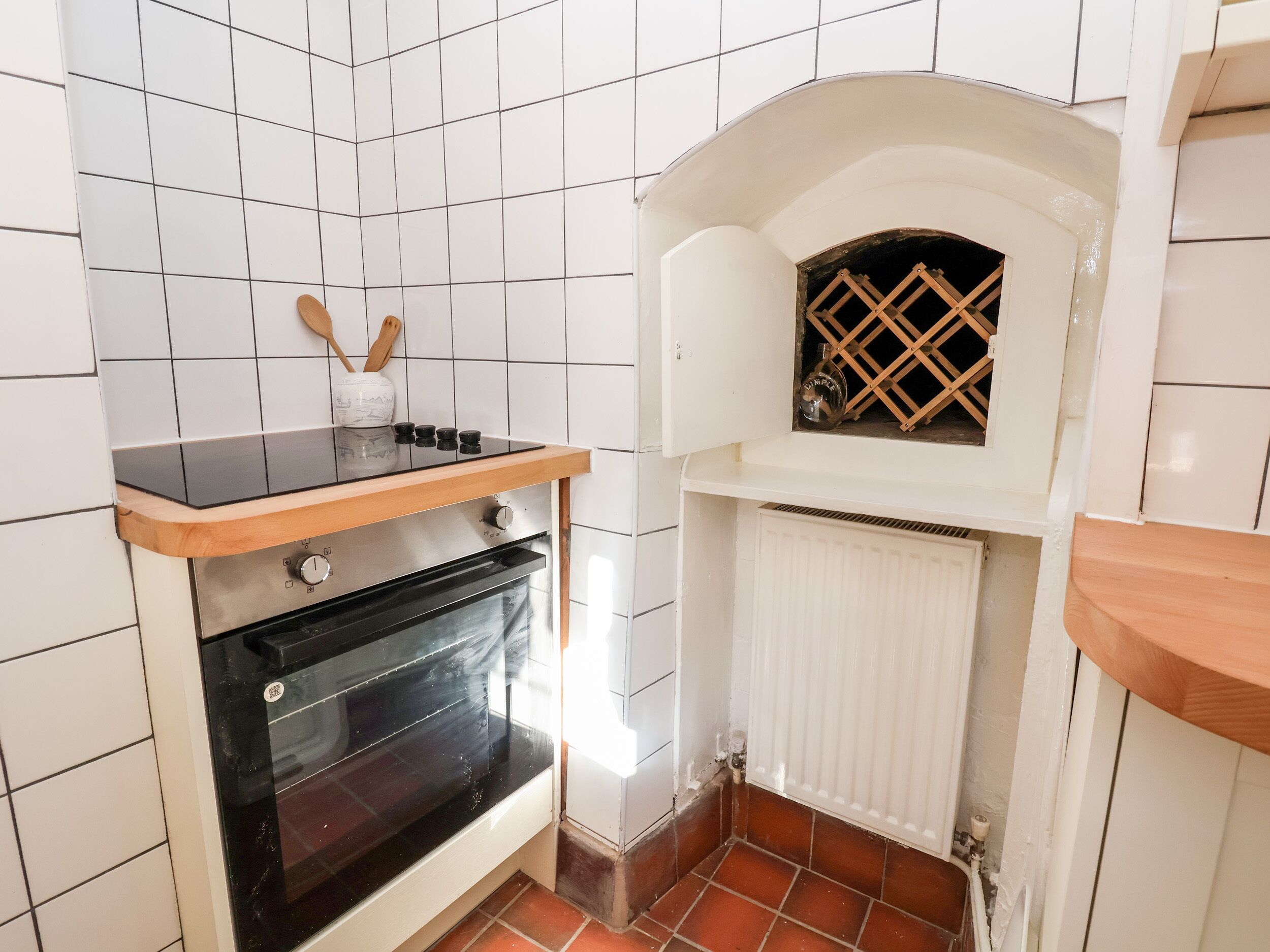 A compact kitchen with white tiled walls, a black oven, and a white radiator.