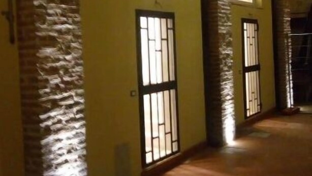 A building with two large windows and a door with metal bars, illuminated by artificial lighting. - Villa Albani welcome house (Roma)