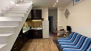 A compact living space with a kitchen, a sofa, and a staircase. - Villa Albani welcome house (Roma)