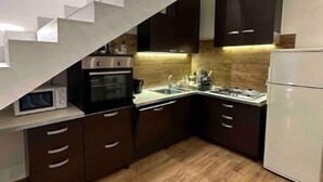 A modern kitchen with a wooden floor, dark cabinets, a microwave, a stove, and a refrigerator. - Villa Albani welcome house (Roma)