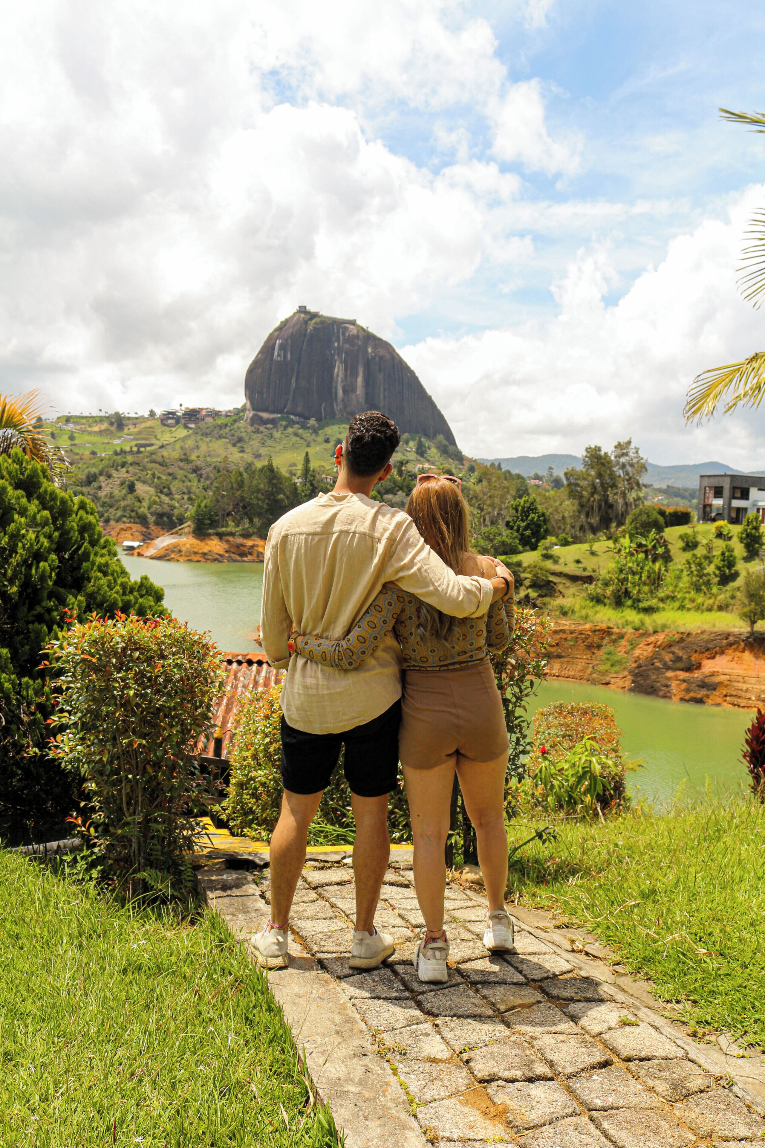 Una pareja parada sobre un sendero de piedra, con vistas a un río y una gran formación rocosa.