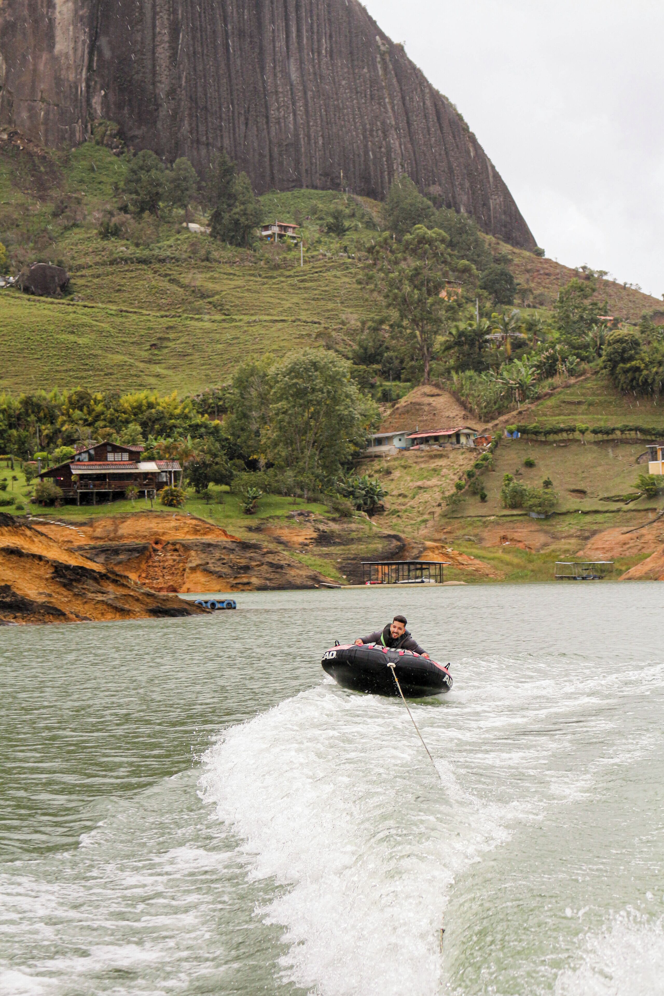 A person wakeboarding on a river with houses and a mountain in the background.